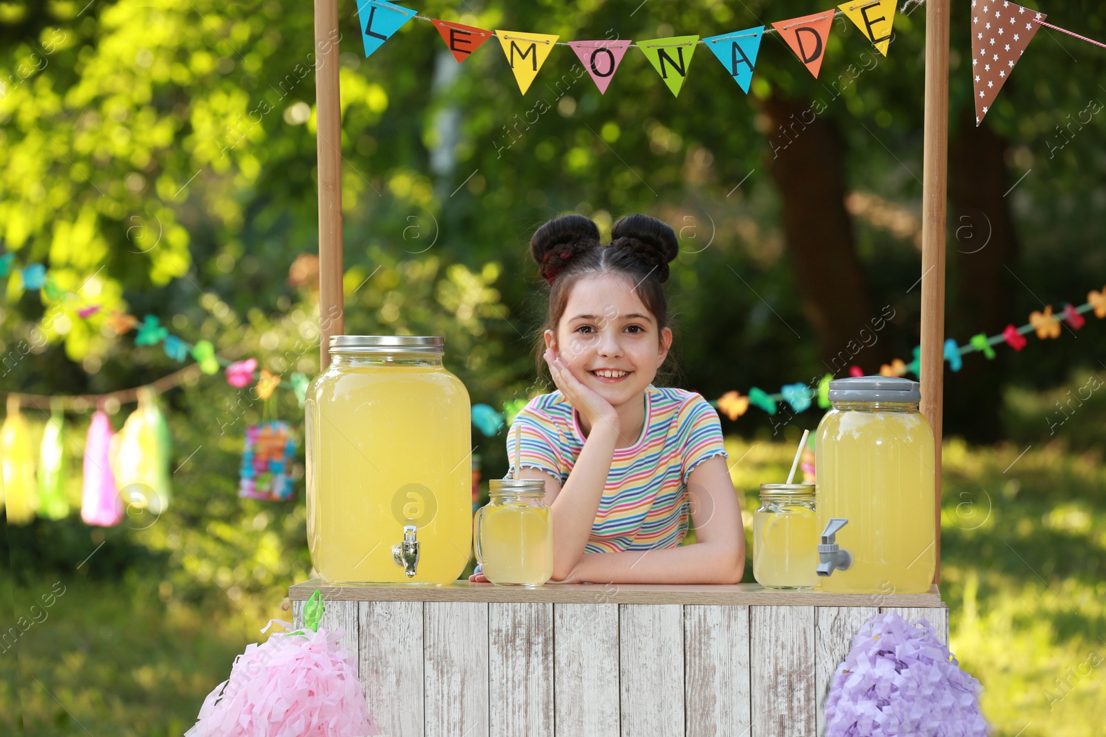 Photo of Cute little girl at lemonade stand in park. Summer refreshing natural drink