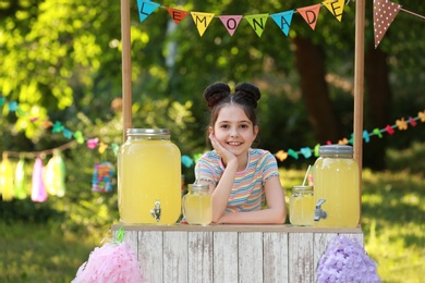 Photo of Cute little girl at lemonade stand in park. Summer refreshing natural drink