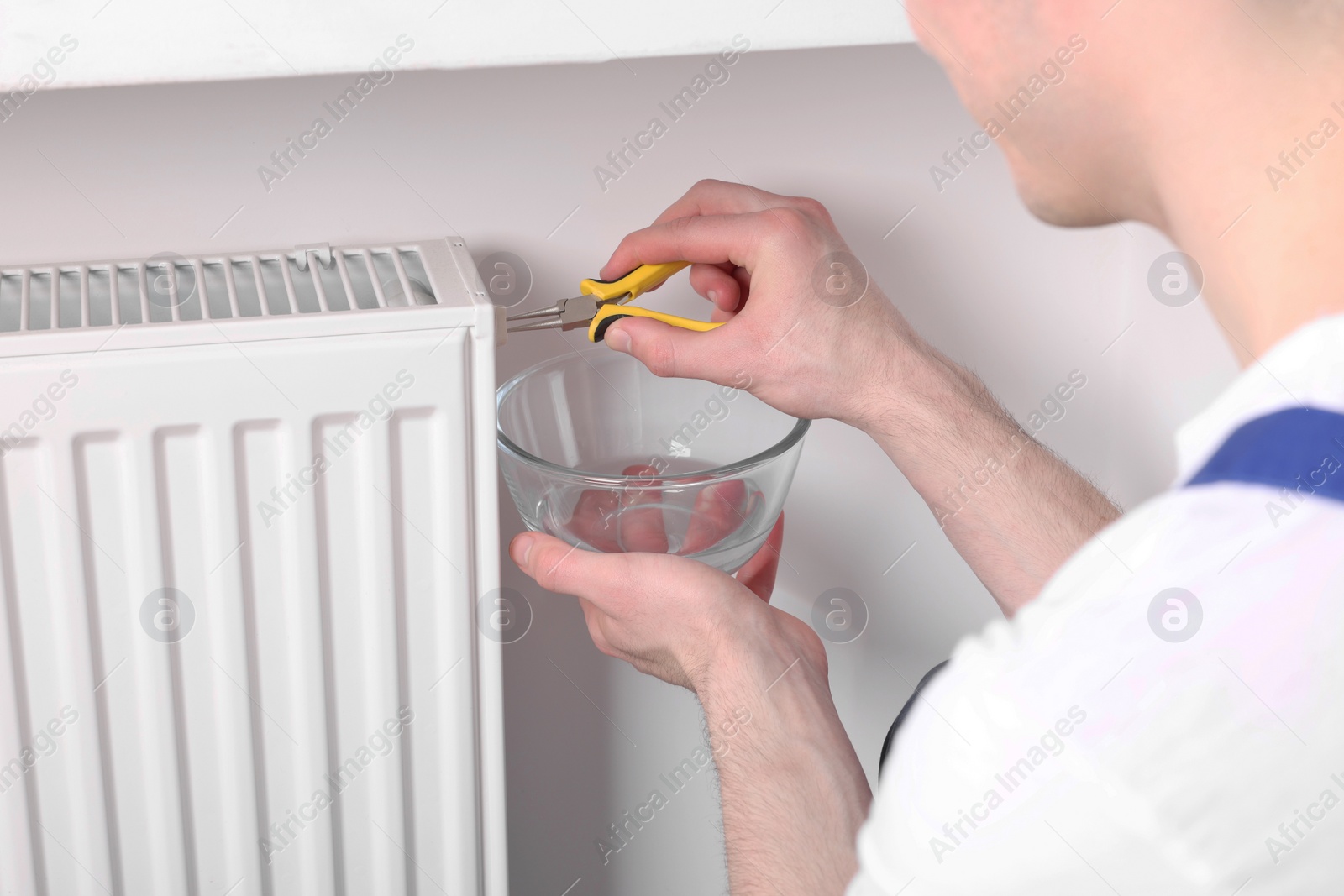 Photo of Professional repairman fixing heating radiator with pliers indoors, closeup