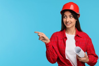 Architect in hard hat with draft pointing at something on light blue background, space for text