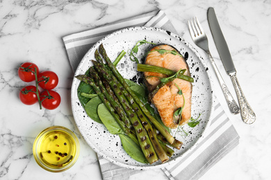 Photo of Tasty salmon steak served with grilled asparagus on white marble table, flat lay