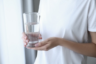 Woman holding glass of water near window at home, closeup