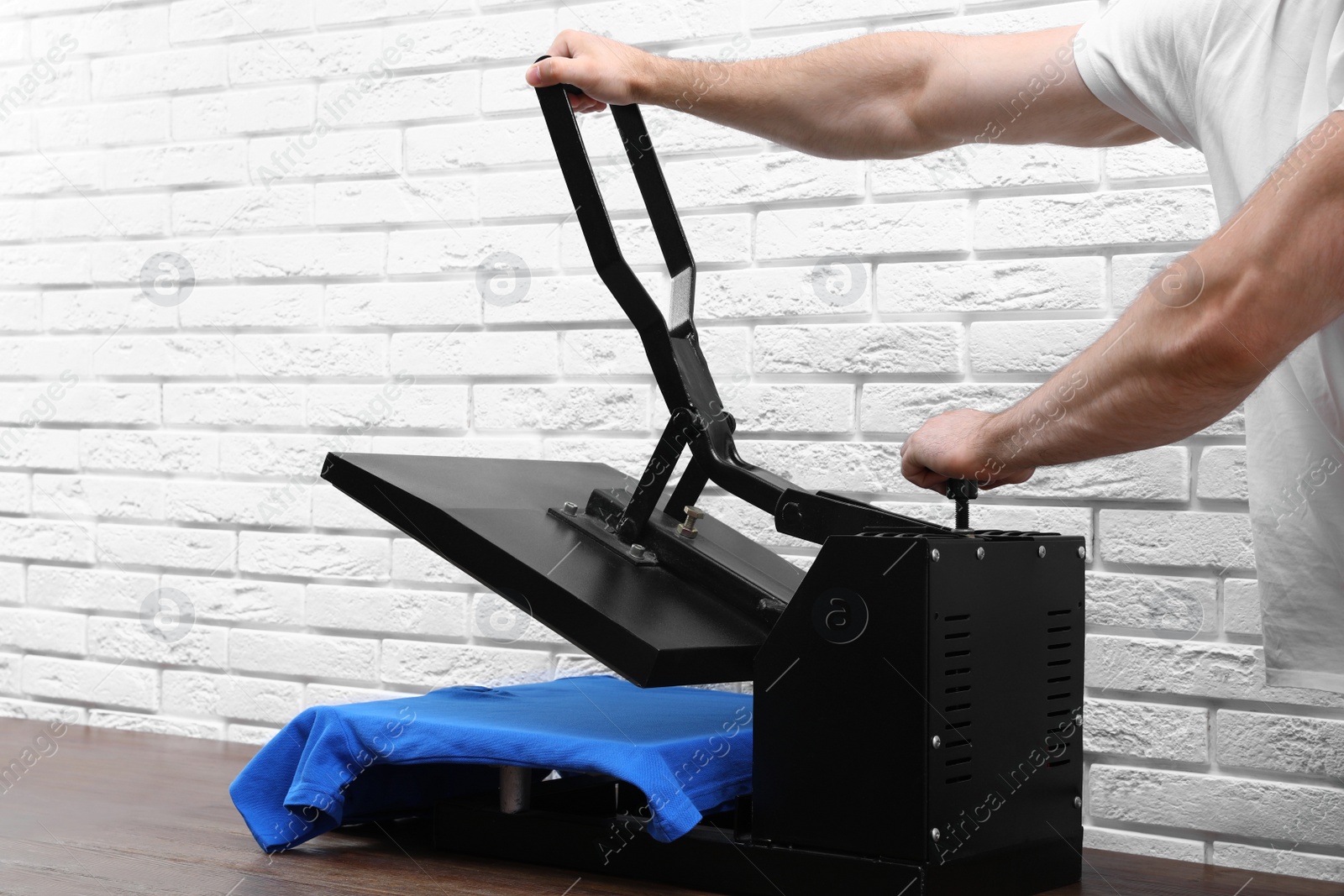 Photo of Man using heat press machine at table near white brick wall, closeup