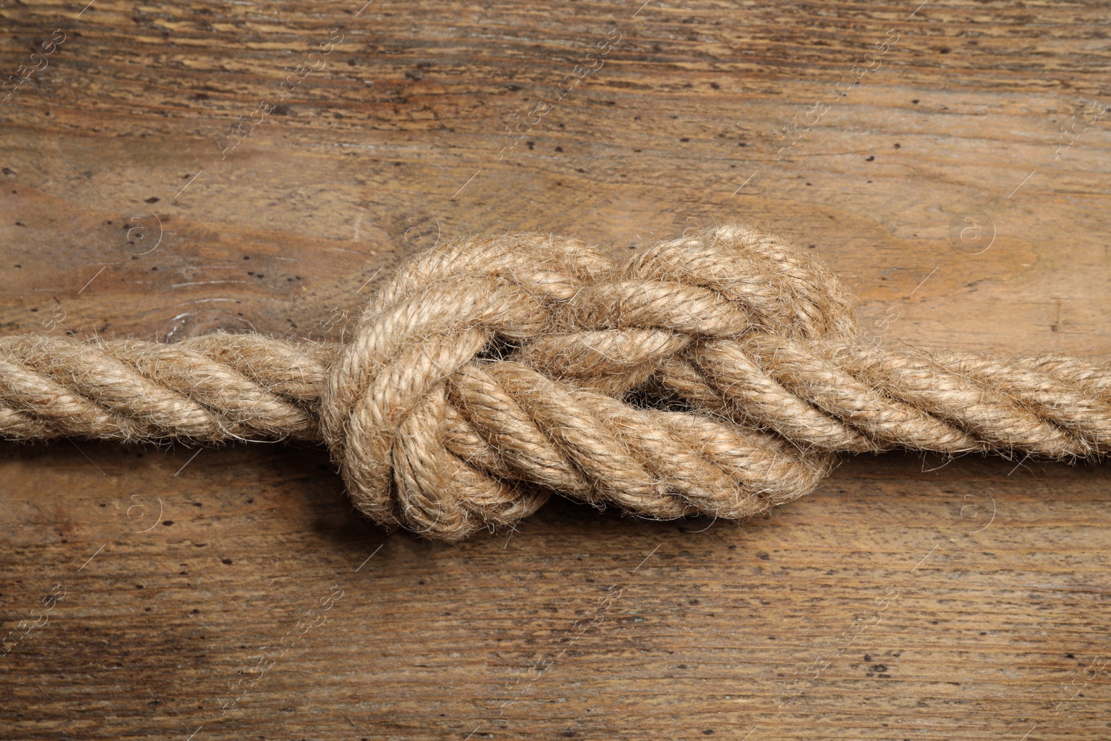 Photo of Linen rope with knot on wooden background, closeup. Unity concept
