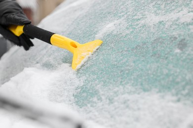 Photo of Man cleaning snow from car windshield outdoors, closeup