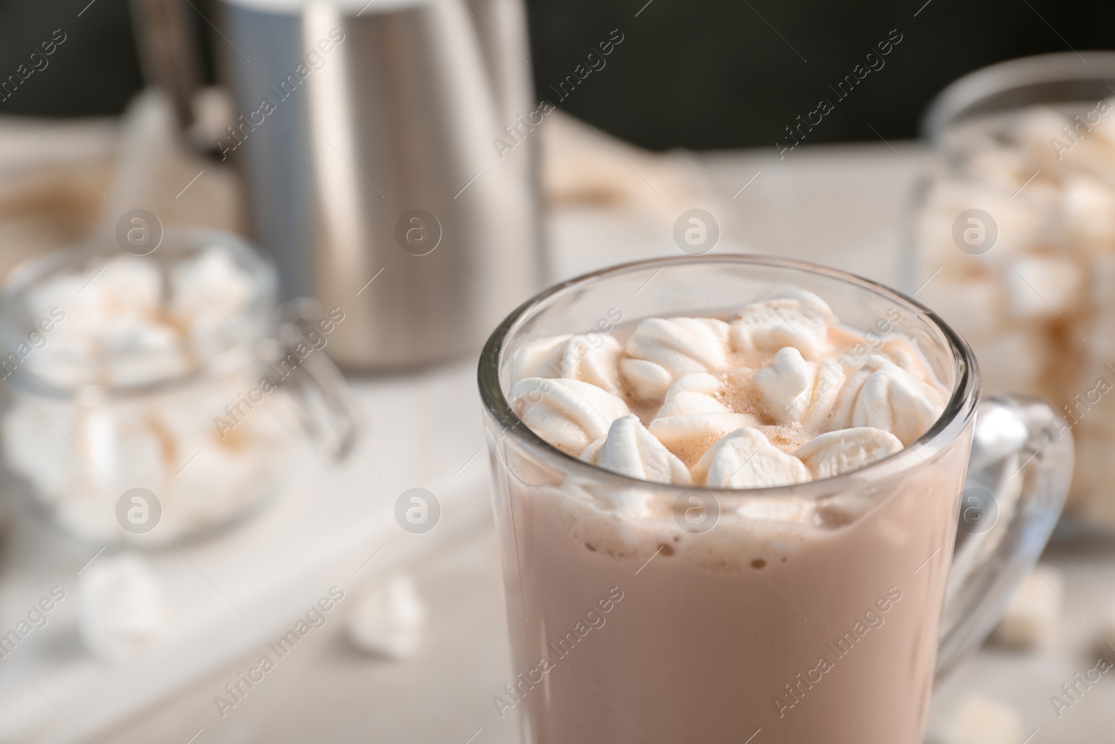 Photo of Tasty hot chocolate with milk and marshmallows in glass cup on table, closeup. Space for text