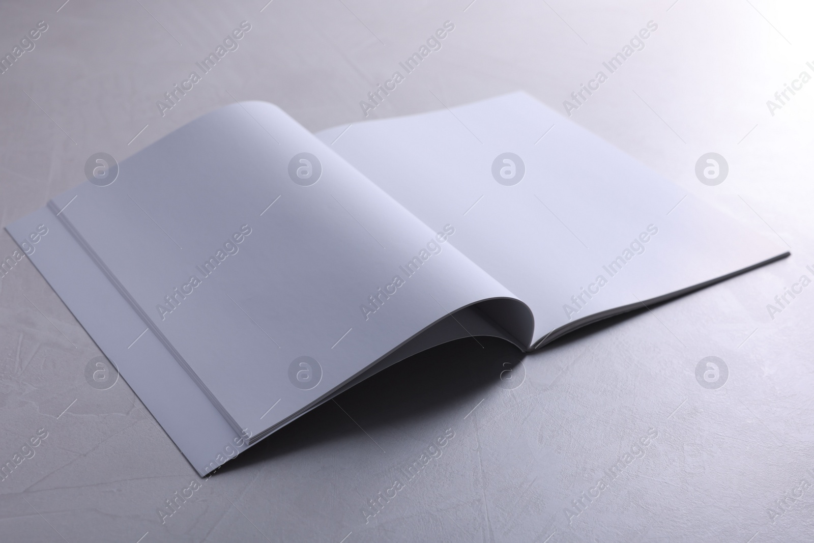 Photo of Open notebook with blank paper sheets on grey textured table. Mockup for design