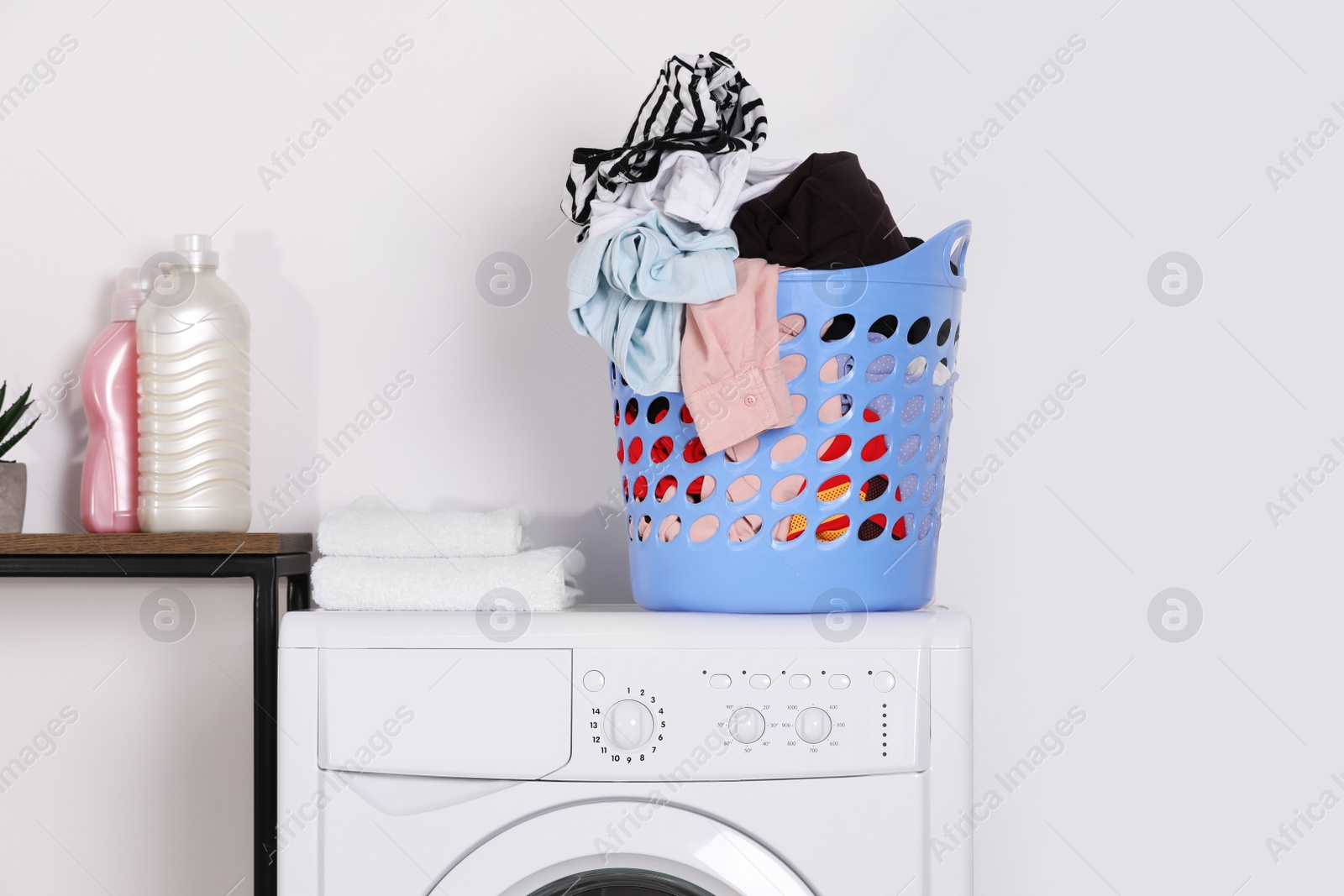 Photo of Laundry basket overfilled with clothes on washing machine in bathroom