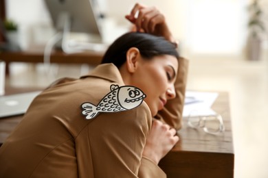 Man sticking paper fish to colleague's back while she sleeping in office, closeup. Funny joke