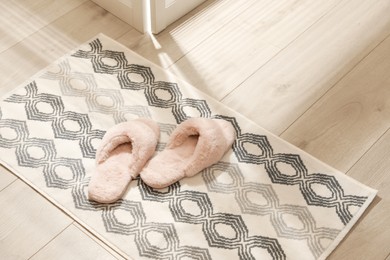 Photo of New stylish bath mat with fluffy slippers on floor indoors