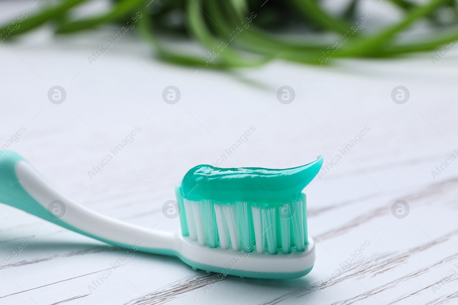 Photo of Brush with toothpaste on white wooden table, closeup