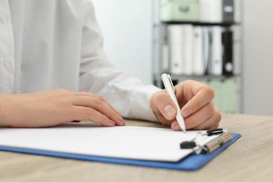 Woman writing in clipboard with pen at wooden table indoors, closeup