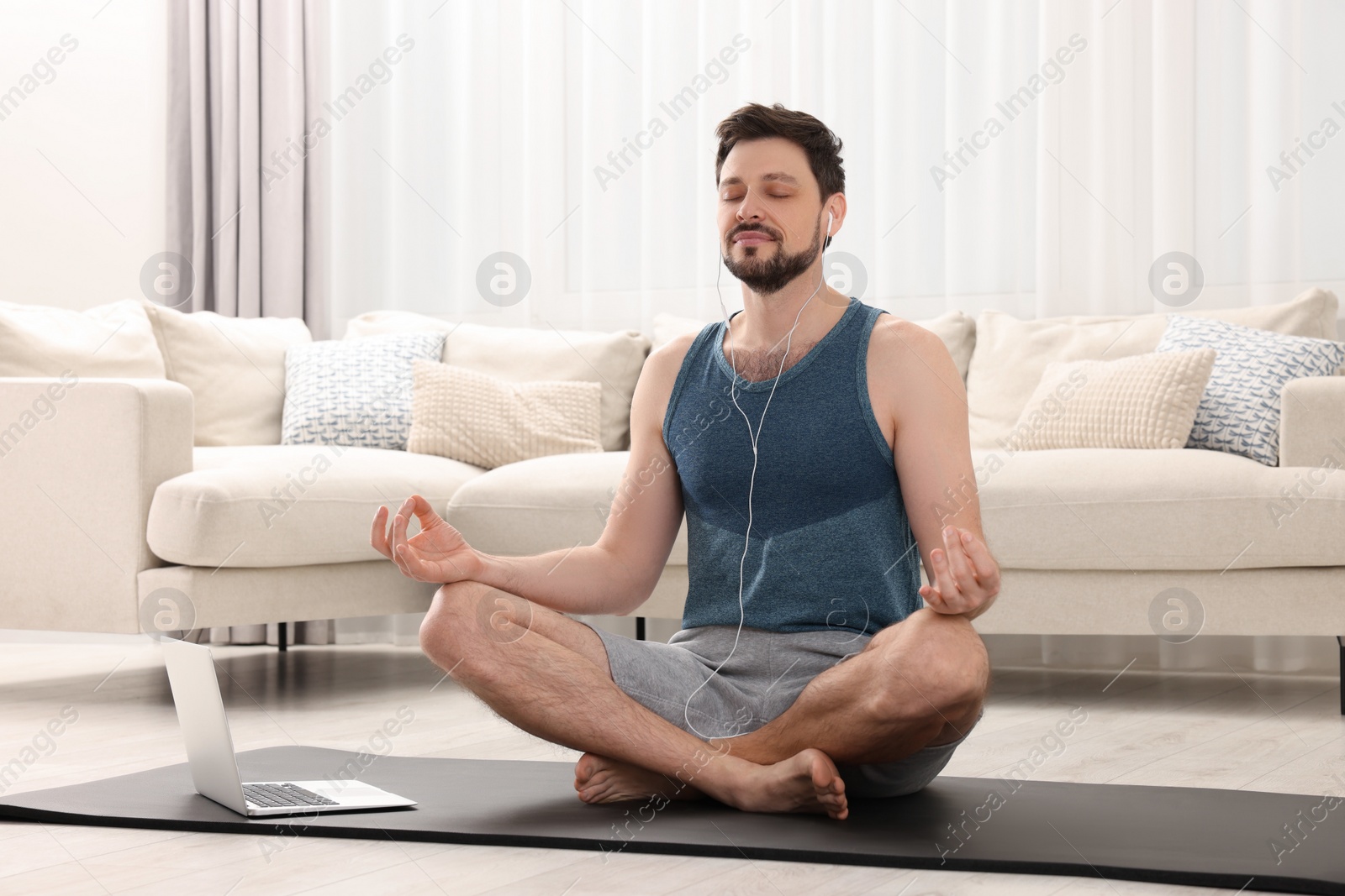 Photo of Man in sportswear meditating near laptop at home. Harmony and zen