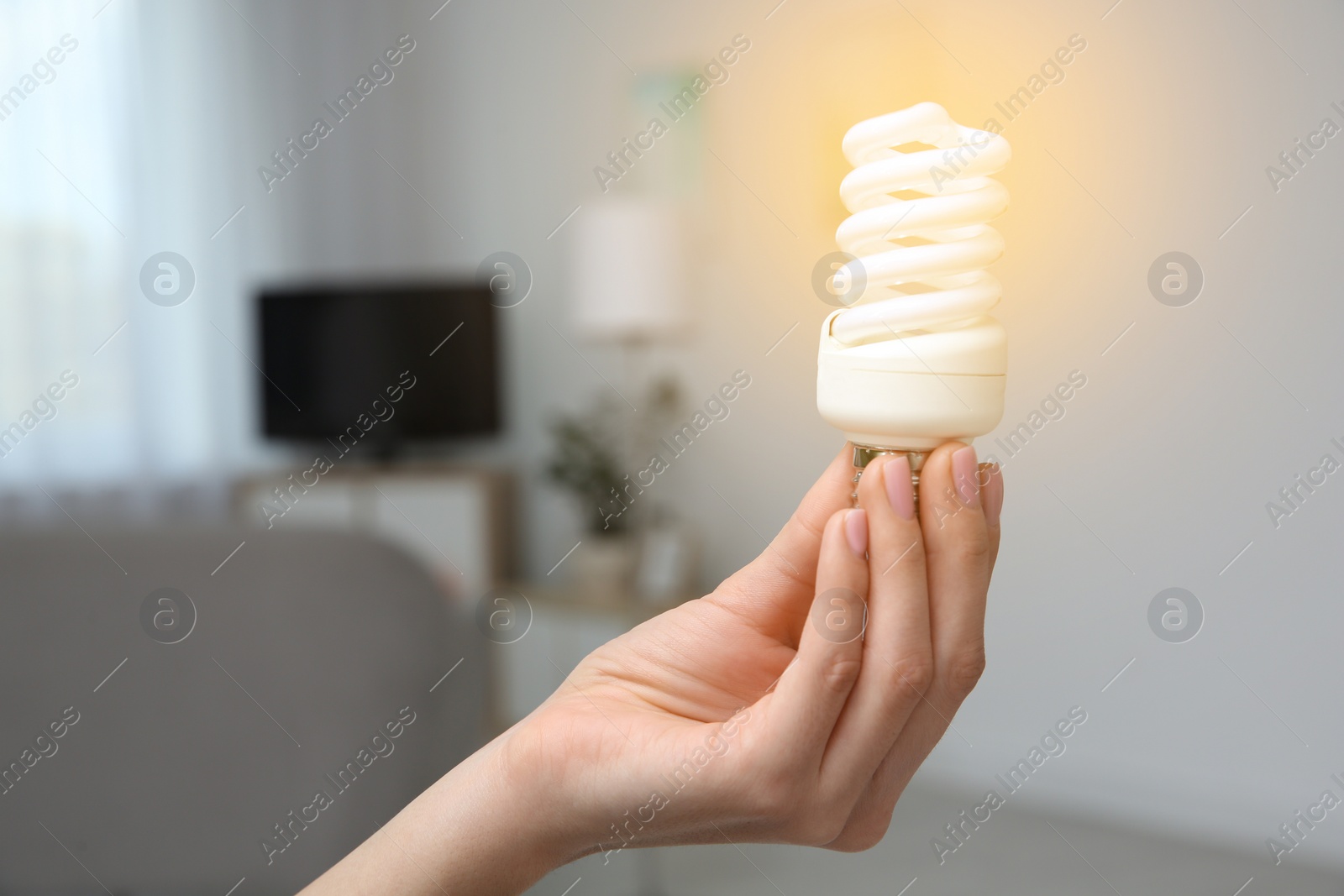 Photo of Woman holding lamp bulb in living room. Space for text