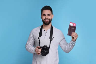 Smiling man with passport, tickets and camera on light blue background