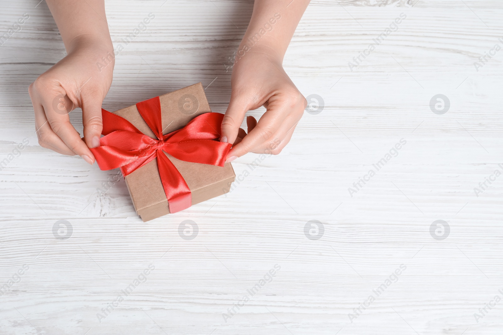 Photo of Woman with gift box at white wooden table, top view. Space for text