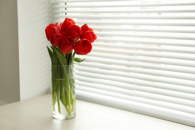 Photo of Window with blinds and beautiful bouquet on sill, space for text