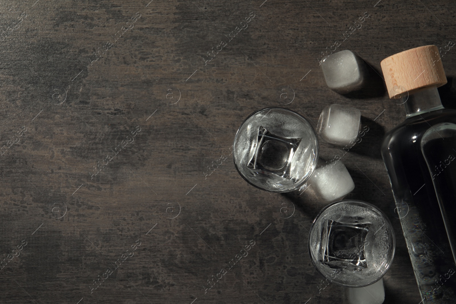 Photo of Bottle of vodka and shot glasses with ice on black table, flat lay. Space for text