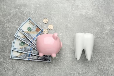 Photo of Ceramic model of tooth, piggy bank and money on grey table, flat lay. Expensive treatment