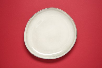 Photo of One ceramic plate on red background, top view