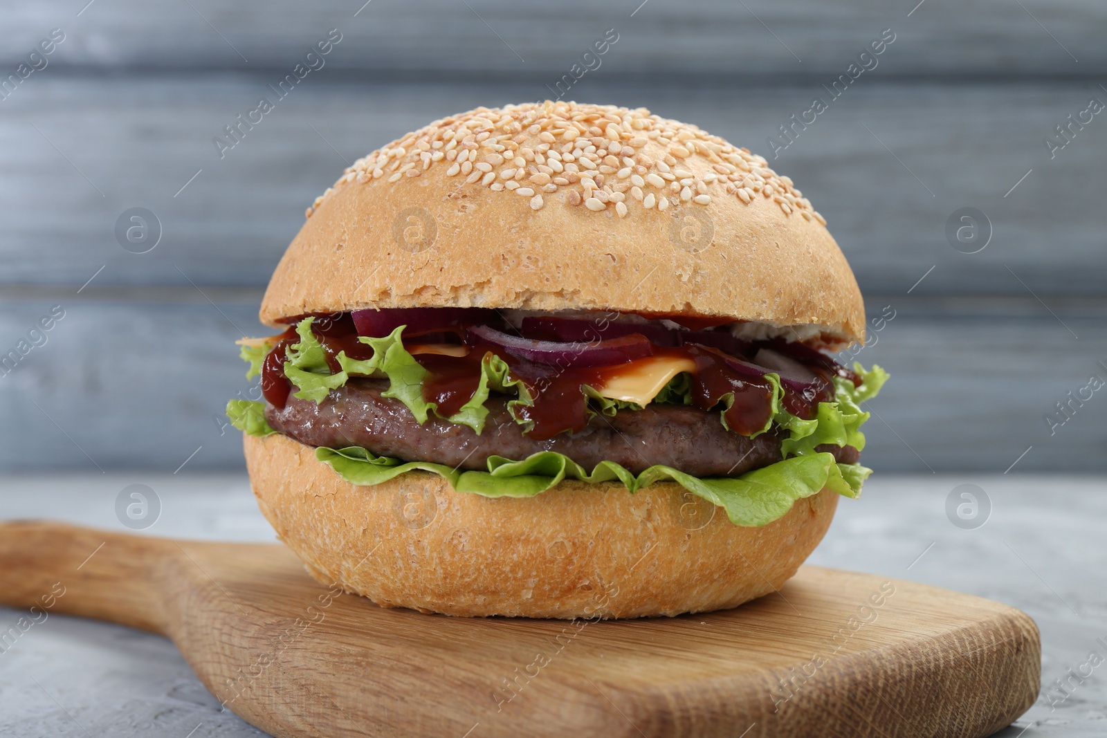 Photo of Delicious cheeseburger with lettuce, onion, ketchup and patty on table, closeup