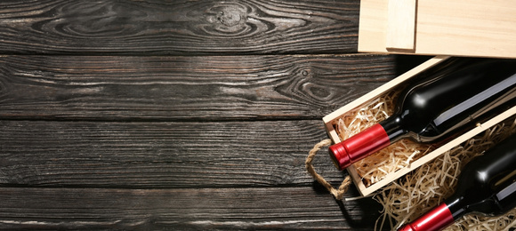 Crate and bottles of wine on wooden table, flat lay with space for text. Banner design