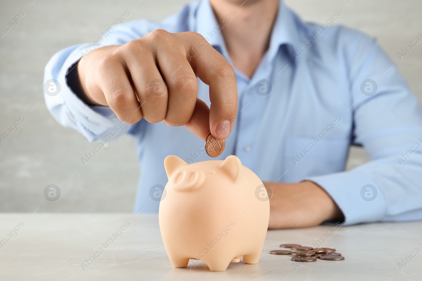 Photo of Man putting coin into piggy bank on grey stone table, closeup view