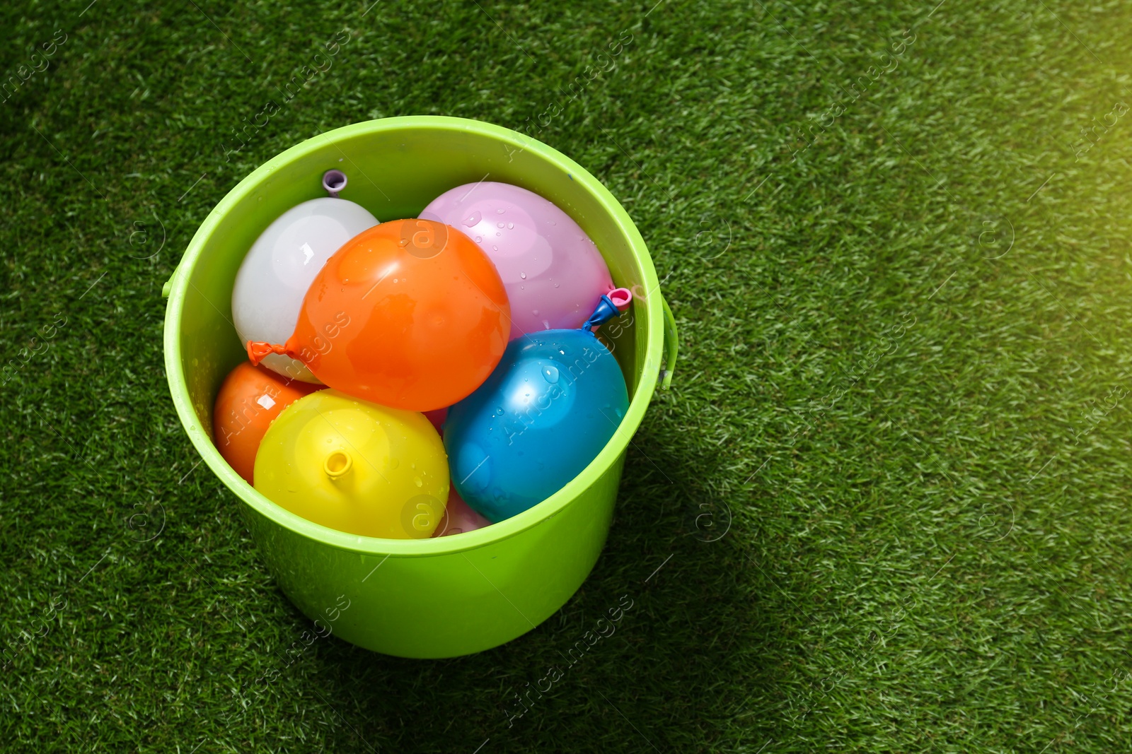 Photo of Bucket full of colorful water bombs on green grass, above view. Space for text