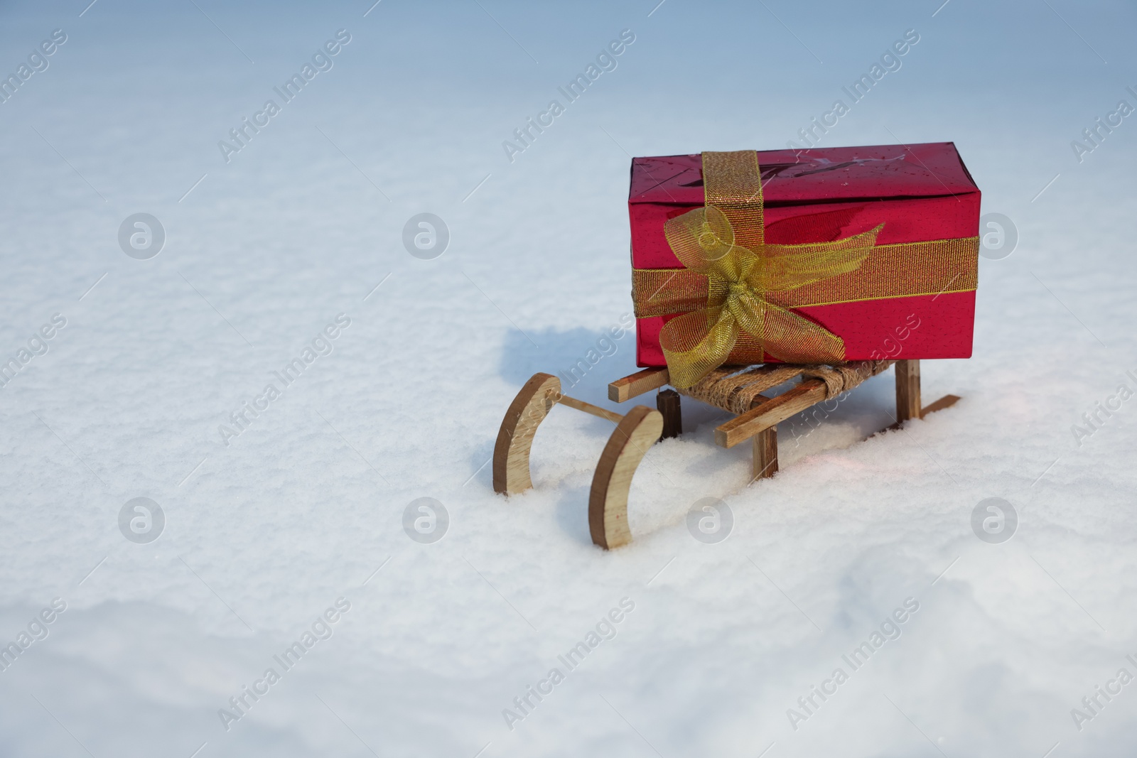 Photo of Wooden sleigh with gift box on snow outdoors. Space for text