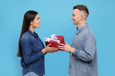 Photo of Lovely couple with beautiful gift box on light blue background. Valentine's day celebration