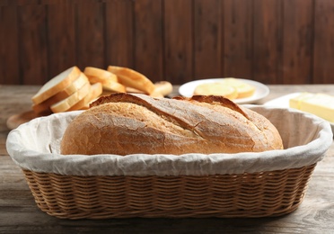 Photo of Loaf of tasty fresh bread in wicker basket on wooden table