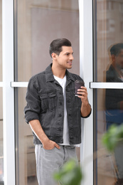 Photo of Handsome man with cup of coffee near window