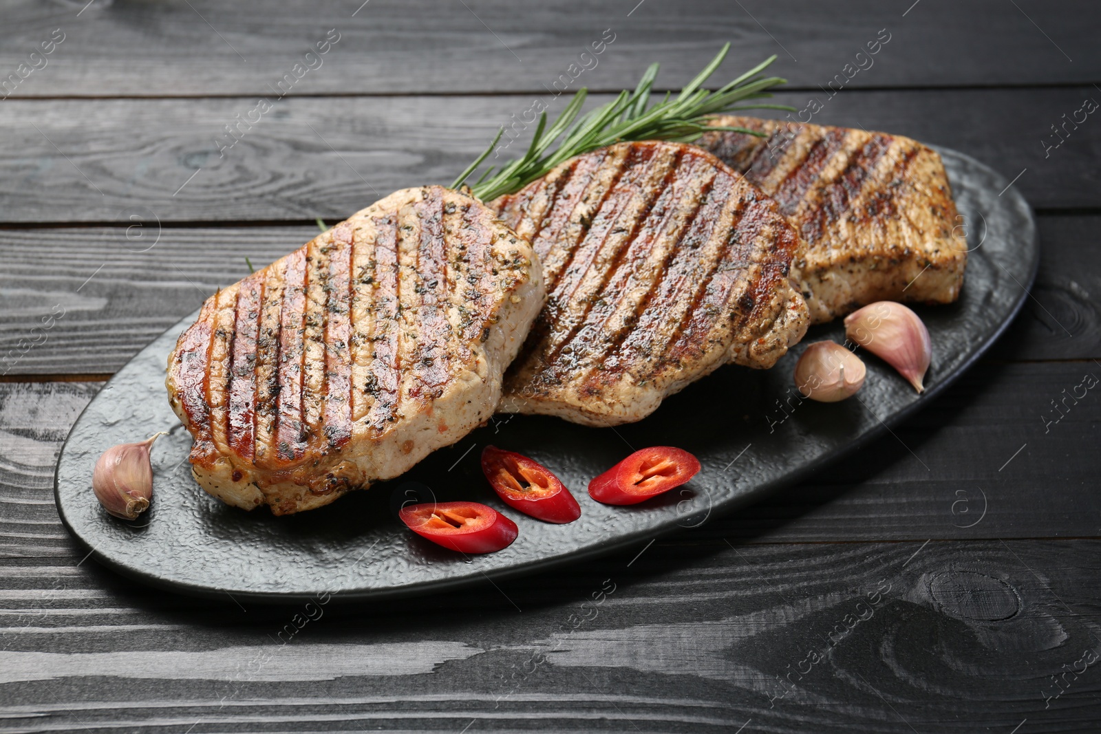 Photo of Delicious grilled pork steaks with spices on dark wooden table