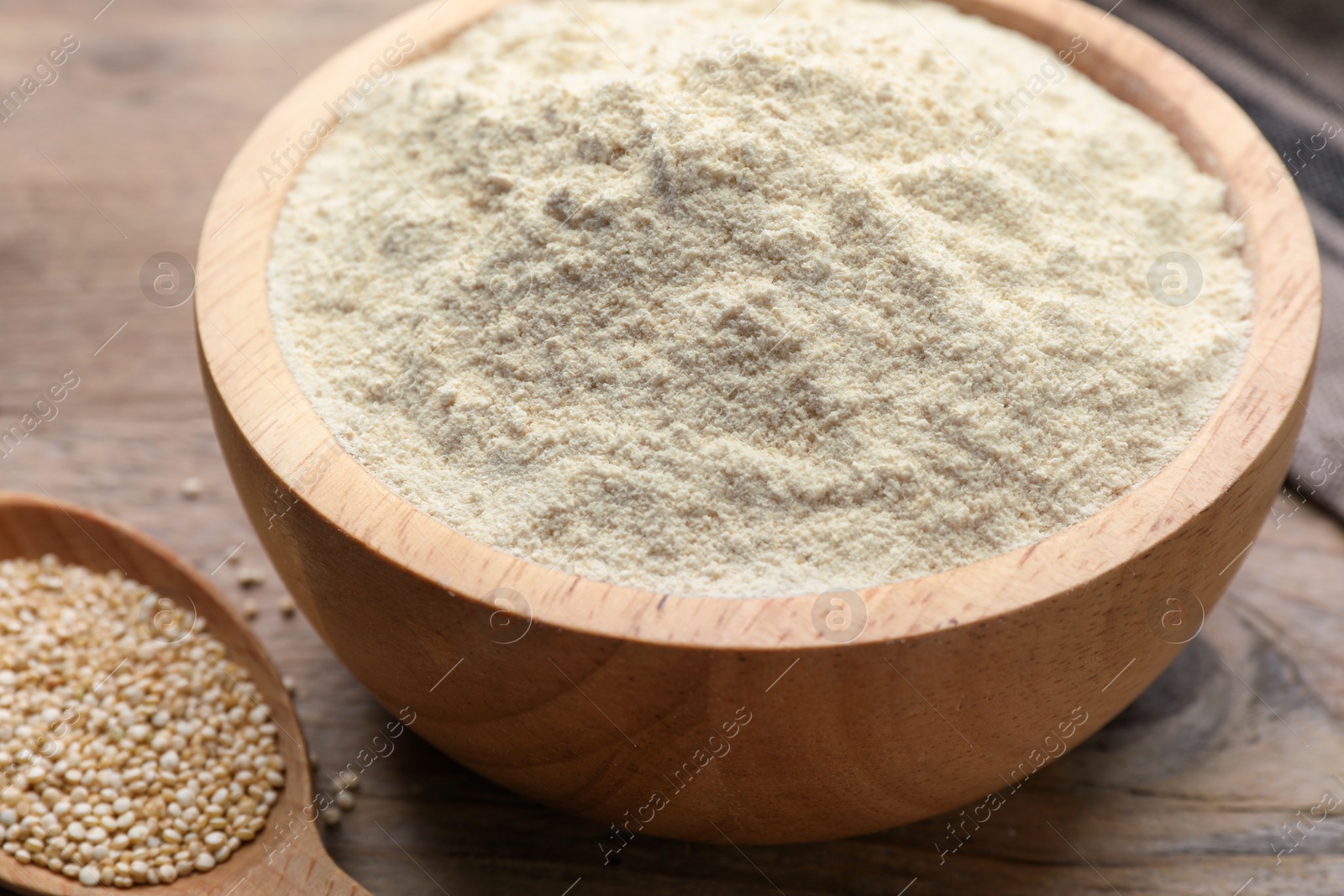 Photo of Quinoa flour in bowl and spoon with seeds on wooden table, closeup