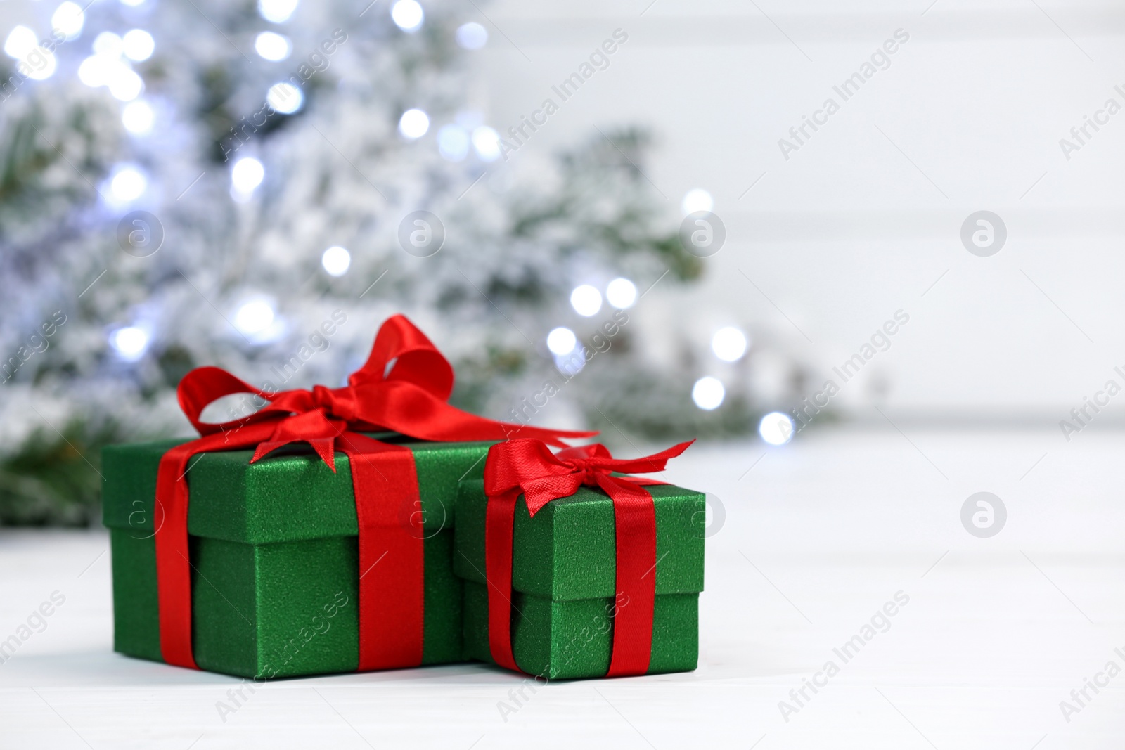 Photo of Beautiful gift boxes on white table against blurred festive lights, space for text. Christmas present