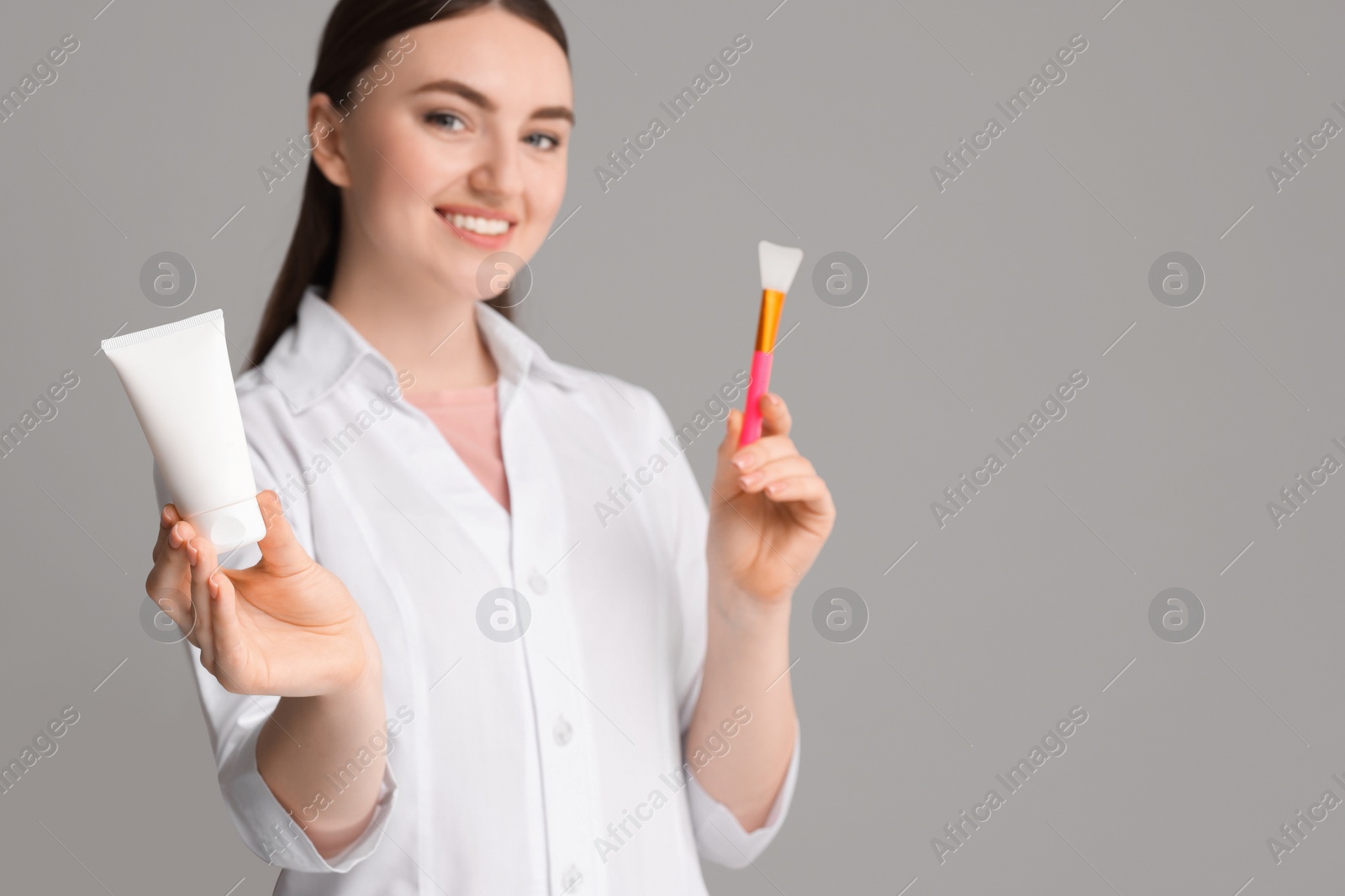 Photo of Cosmetologist with cosmetic product and silicone brush on grey background, selective focus. Space for text