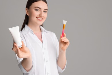 Cosmetologist with cosmetic product and silicone brush on grey background, selective focus. Space for text