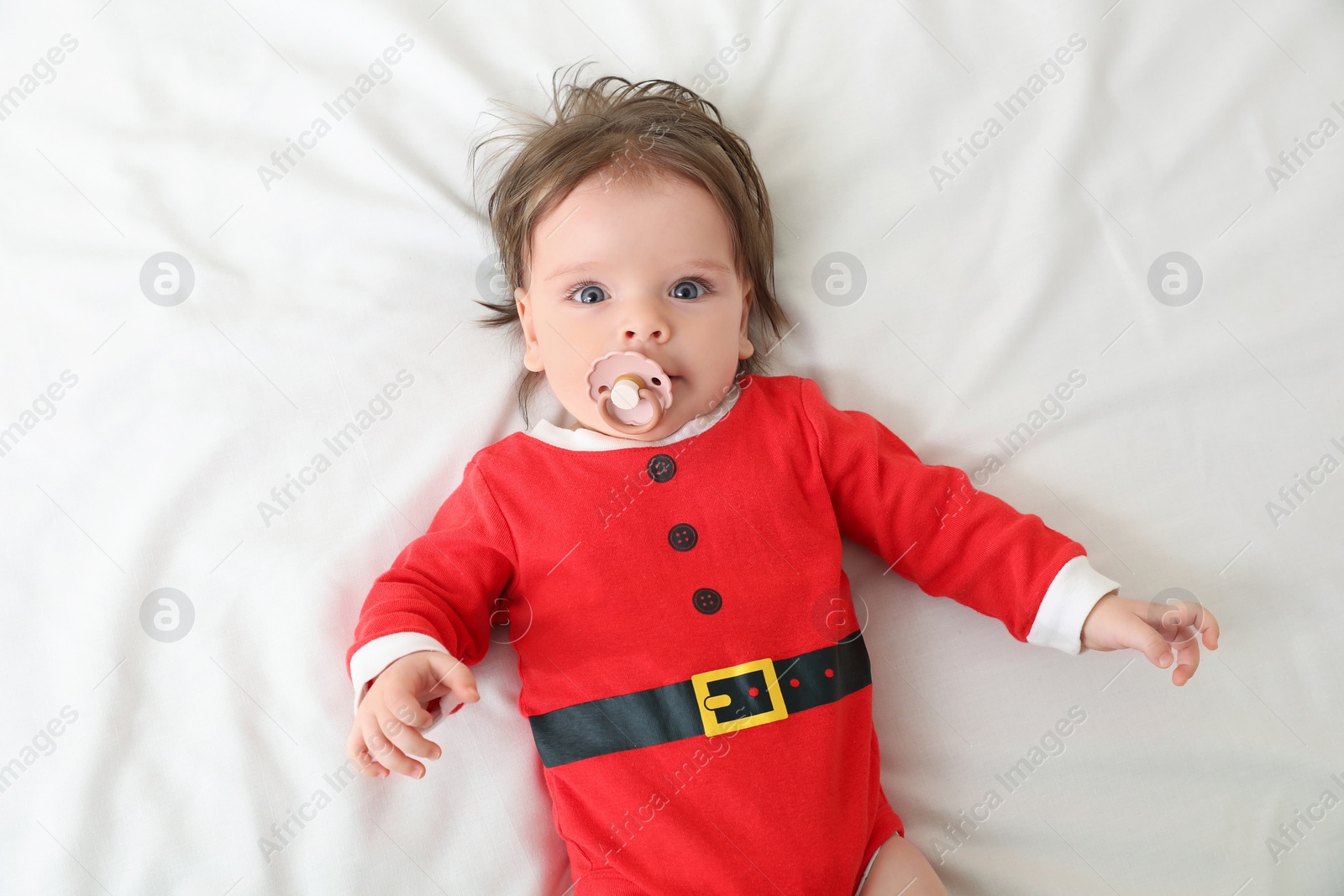 Photo of Cute baby wearing festive Christmas costume with pacifier on white bedsheet, top view