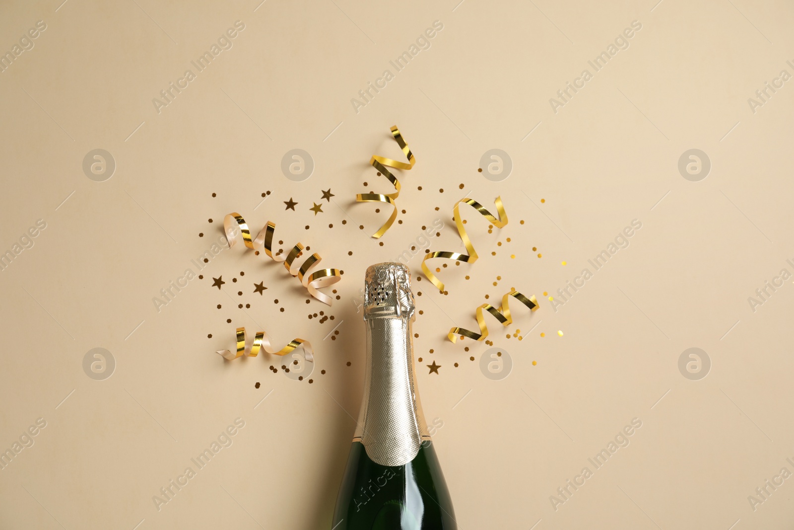 Photo of Bottle of champagne with gold glitter and confetti on beige background, flat lay. Hilarious celebration