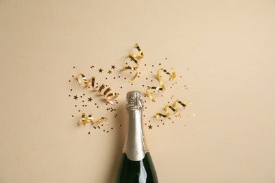 Photo of Bottle of champagne with gold glitter and confetti on beige background, flat lay. Hilarious celebration