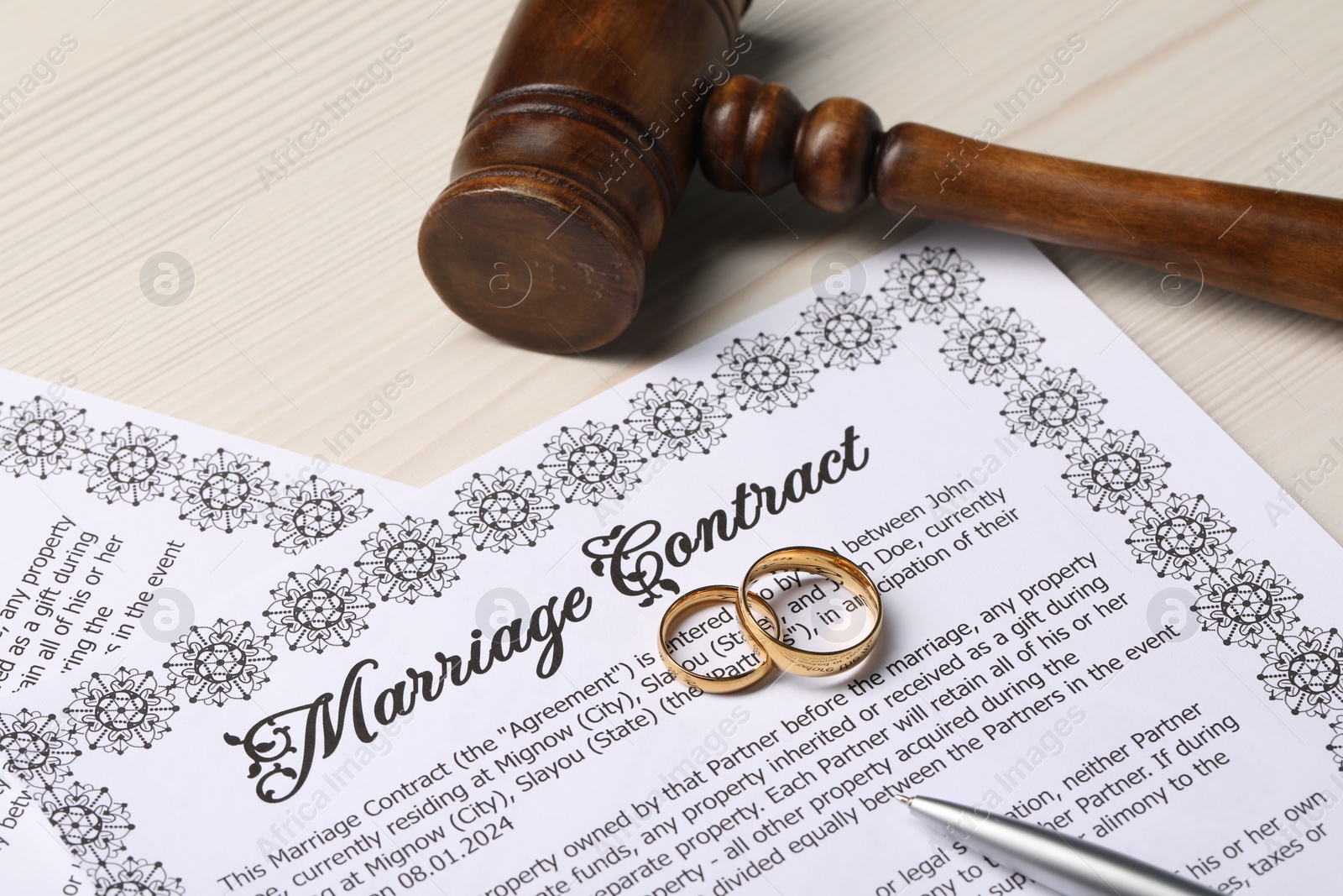 Photo of Marriage contracts, gold rings, pen and gavel on light wooden table, closeup