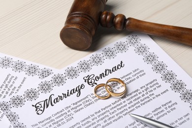 Photo of Marriage contracts, gold rings, pen and gavel on light wooden table, closeup