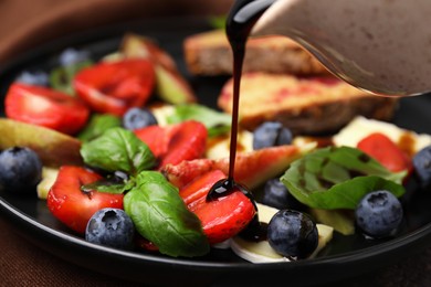 Pouring balsamic vinegar onto fresh salad with blueberries, strawberries and basil on plate, closeup