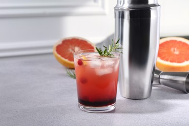 Delicious cocktail, grapefruit and bartender equipment on light grey table, space for text