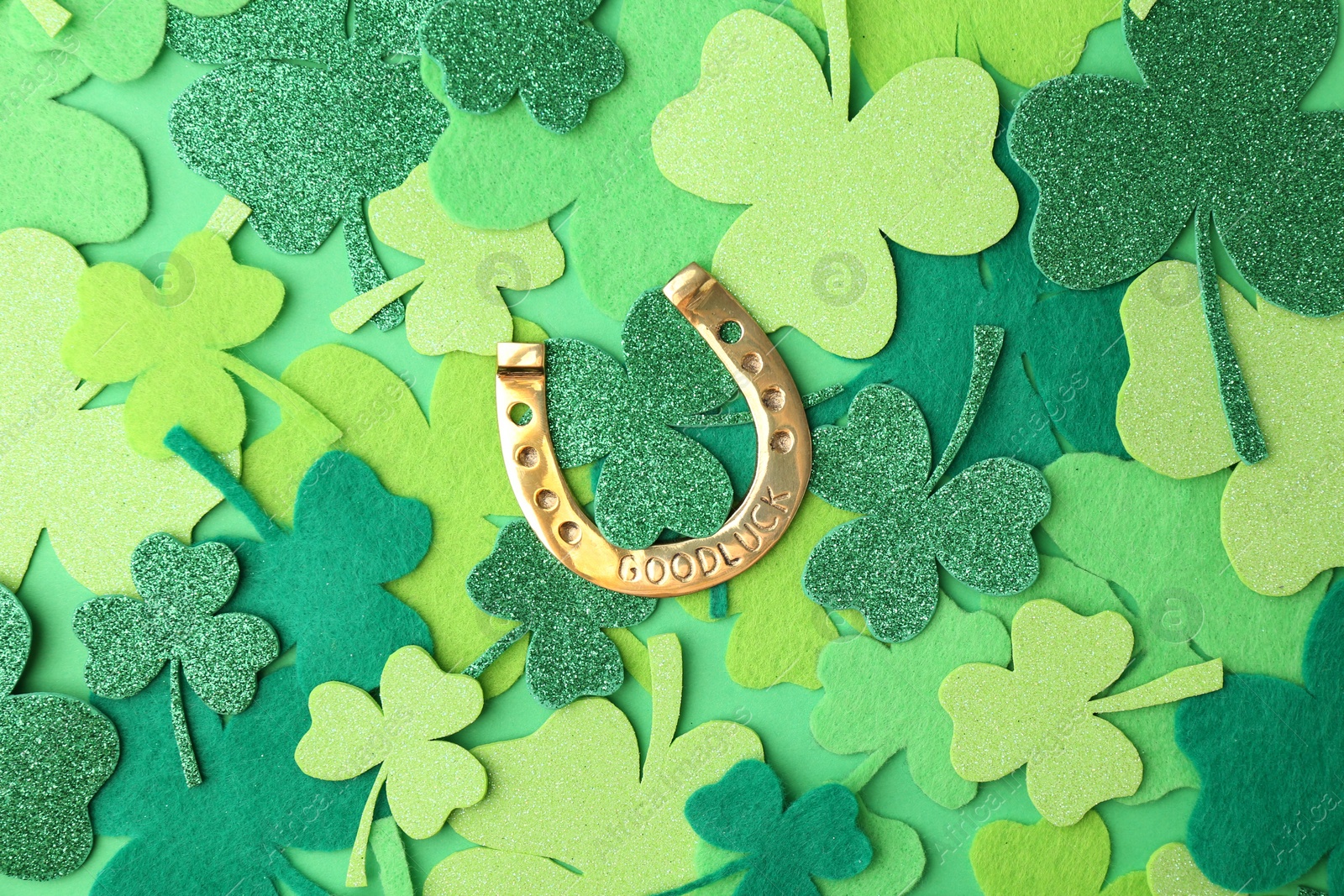 Photo of St. Patrick's day. Golden horseshoe and decorative clover leaves on green background, flat lay