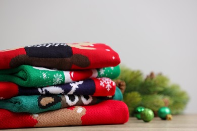 Photo of Stack of different Christmas sweaters, fir tree branch and baubles on table. Space for text