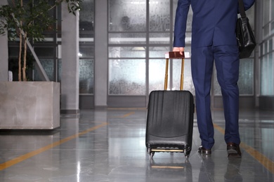 Photo of Businessman with black travel suitcase in airport. Space for text