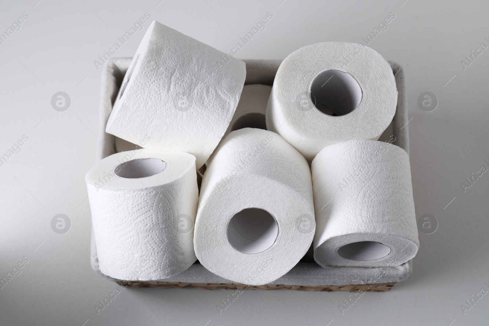 Photo of Toilet paper rolls in basket on white table, top view