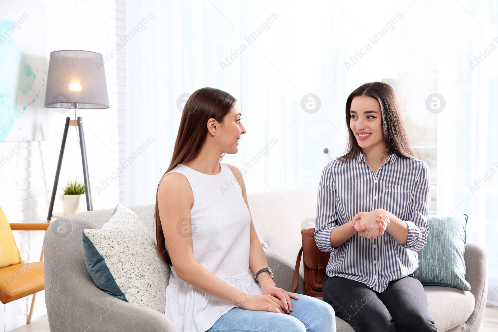 Photo of Hearing impaired friends using sign language for communication on sofa in living room