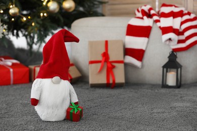 Cute Scandinavian gnome with gift box on carpet near Christmas tree in room